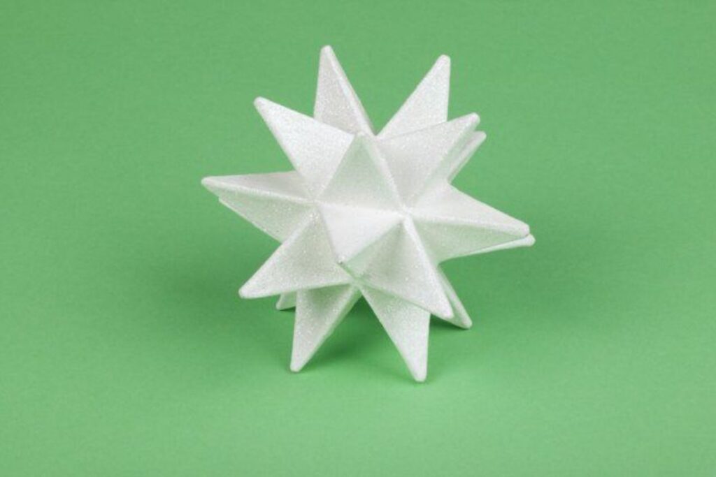 A white, eight-pointed paper Moravian Star against a solid green background, featuring sharp, clean edges and a geometric design.