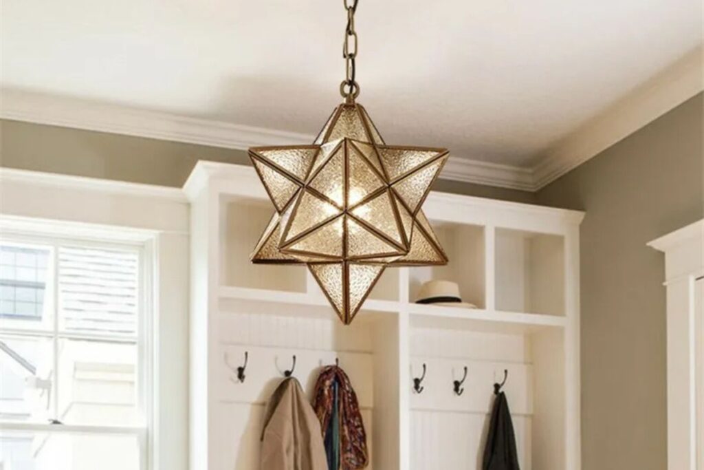 "A hanging glass Moravian Star light with a golden frame, casting a warm glow through its transparent geometric panels.