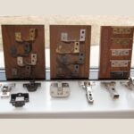 Various types of hidden cabinet hinges displayed on wooden boards, showcasing different designs and finishes. The hinges are arranged for easy comparison, including several metal finishes and mechanisms that are typically used for modern, concealed cabinetry solutions.