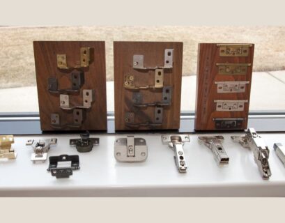 Various types of hidden cabinet hinges displayed on wooden boards, showcasing different designs and finishes. The hinges are arranged for easy comparison, including several metal finishes and mechanisms that are typically used for modern, concealed cabinetry solutions.