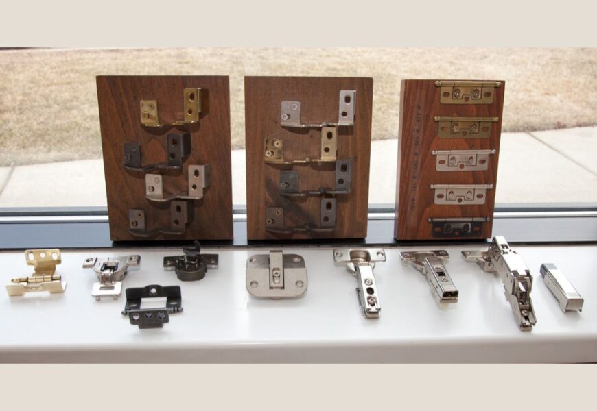 Various types of hidden cabinet hinges displayed on wooden boards, showcasing different designs and finishes. The hinges are arranged for easy comparison, including several metal finishes and mechanisms that are typically used for modern, concealed cabinetry solutions.